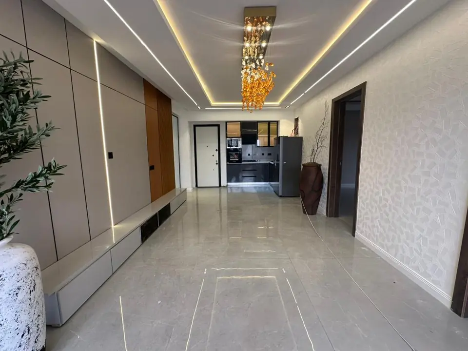 Long hallway towards the kitchen with LED lines in the ceiling, panelled walls and large floor tiles