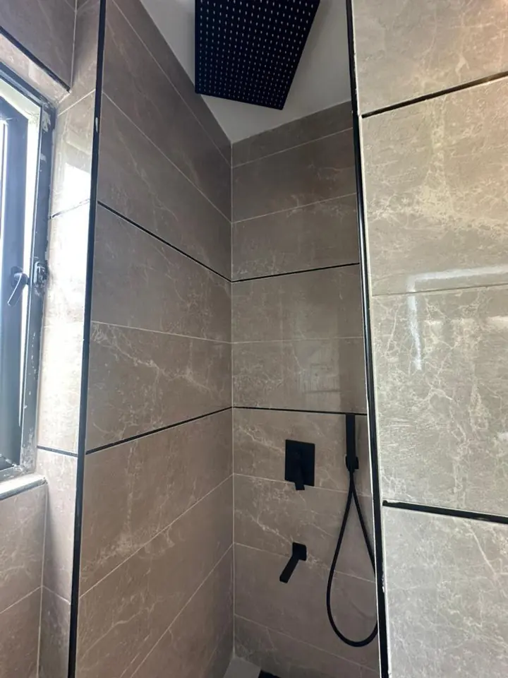 Shower with large-format tiles, black fittings and a handheld shower