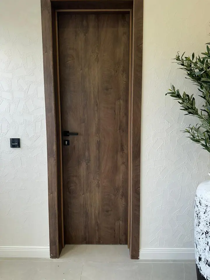 Timber-finish door with a black handle set in a textured white wall